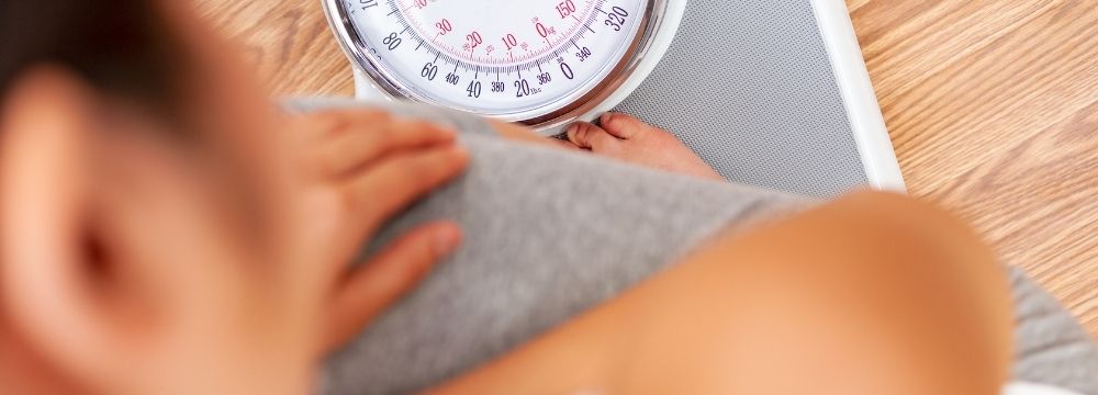Woman stepping on scale, wooden floor, staring at number on scale 