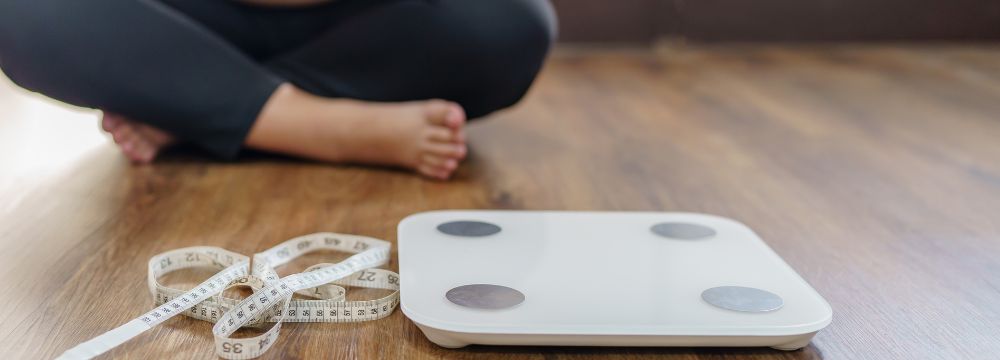 woman sitting on floor behind floor scale and measuring tape on floor