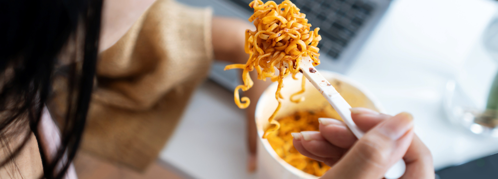 Woman eating high sodium cup of noodles with plastic fork 