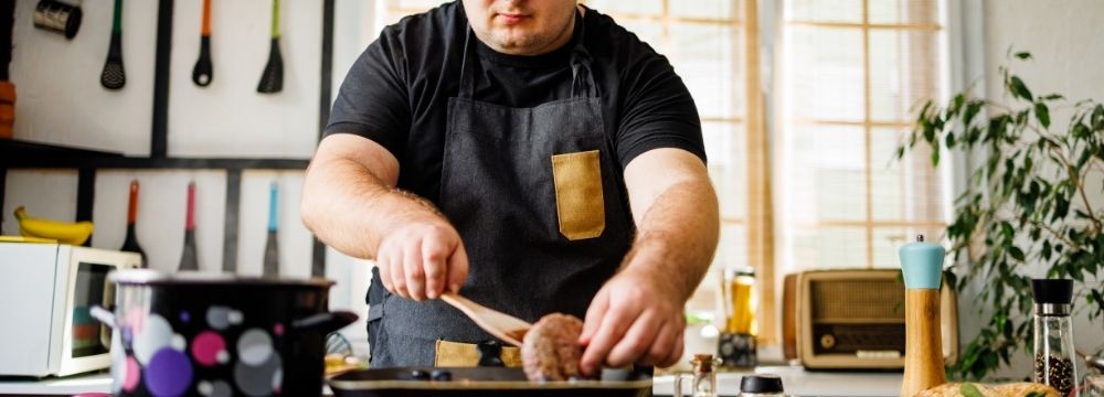 Obese man flipping meat patty while cooking in kitchen