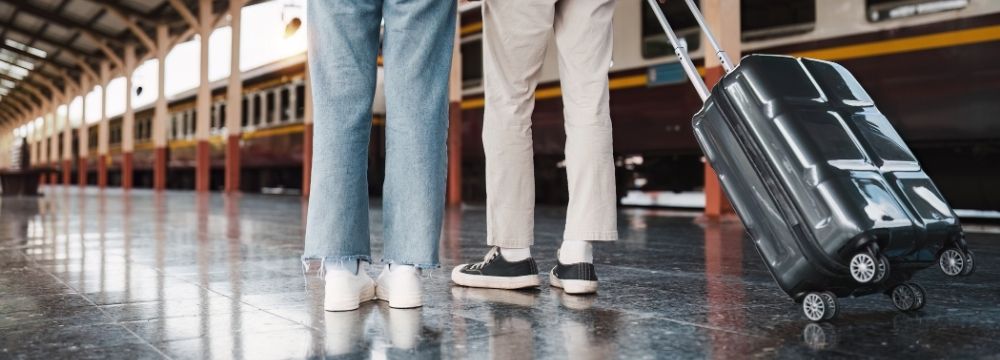 Bottom half of man pulling a suitcase at train station next to travel partner 