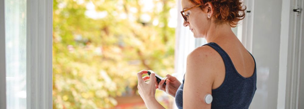 woman with glucose monitor on arm checking her glucose levels on phone