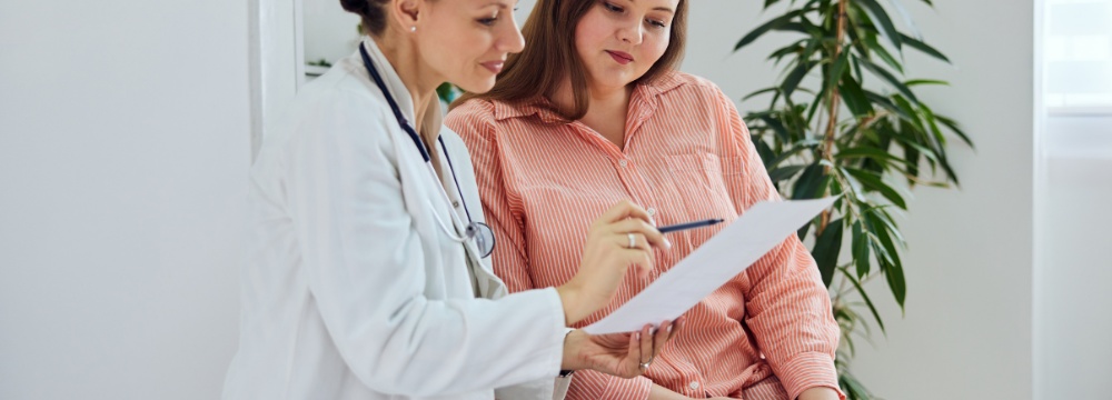 Woman looking at paperwork with doctor holding pen and pointing to paperwork 