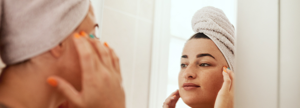 Woman looking in bathroom mirror touching face with both hands 